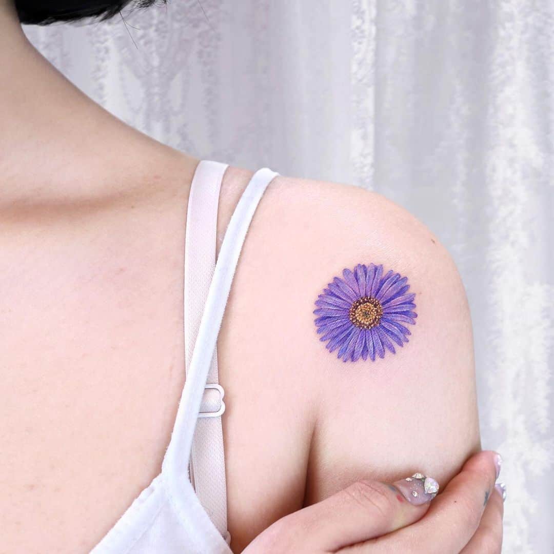 Colored aster flower tattoo on shoulder by plette.tt